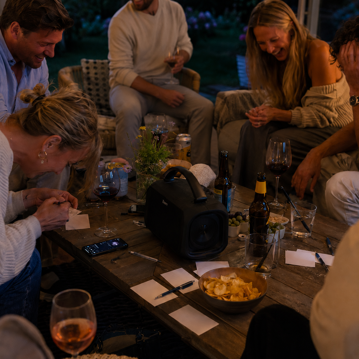 Vänner samlade runt bordet med högtalare under ett musikquiz i sommarkvällen